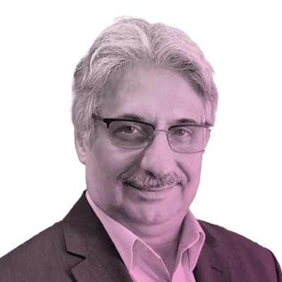 A middle-aged man with gray hair, glasses, and a mustache is wearing a suit jacket and collared shirt, facing the camera and smiling slightly. The image has a pink tint.